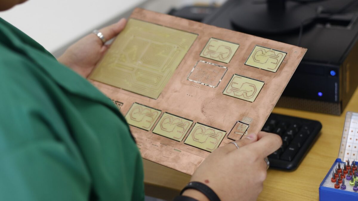 Leiterplatten-Layout auf einem Bildschirm neben einer bestückten Platine