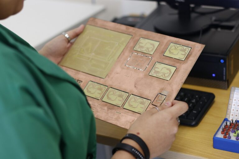 Leiterplatten-Layout auf einem Bildschirm neben einer bestückten Platine