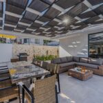 Moderne Terrassenüberdachung aus Glas und Aluminium über einem Sitzplatz im Garten