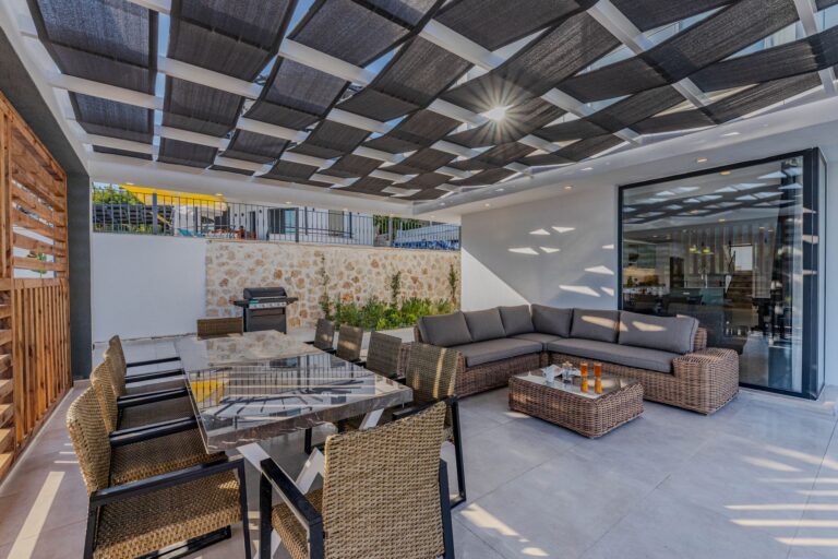 Moderne Terrassenüberdachung aus Glas und Aluminium über einem Sitzplatz im Garten